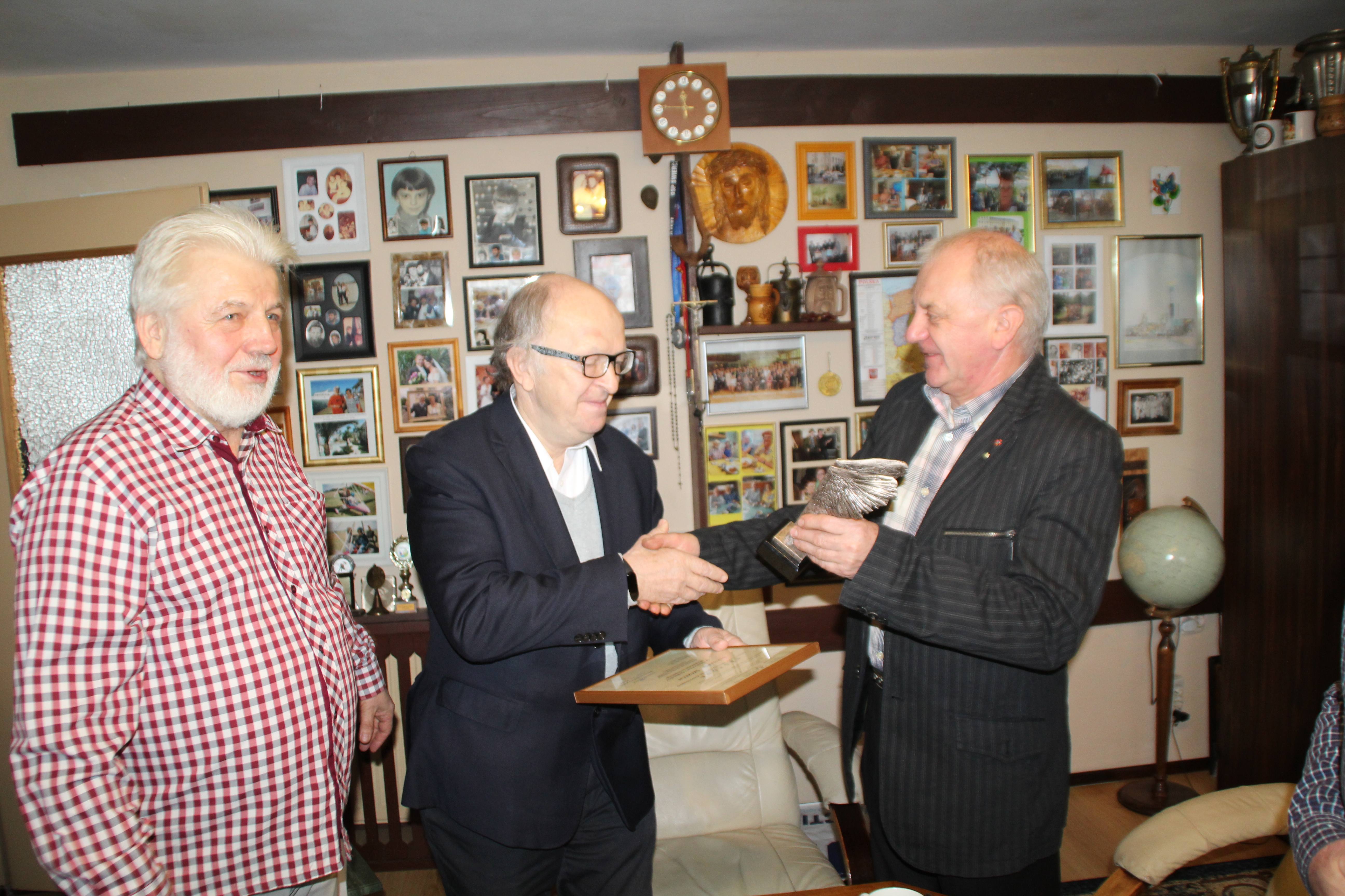 Wręczenie nagrody laureatowi, na zdjęcu trzech mężczyzn. Na środku stoi laureat, który ściska dłoń przedstawiciela organizatora nagrody