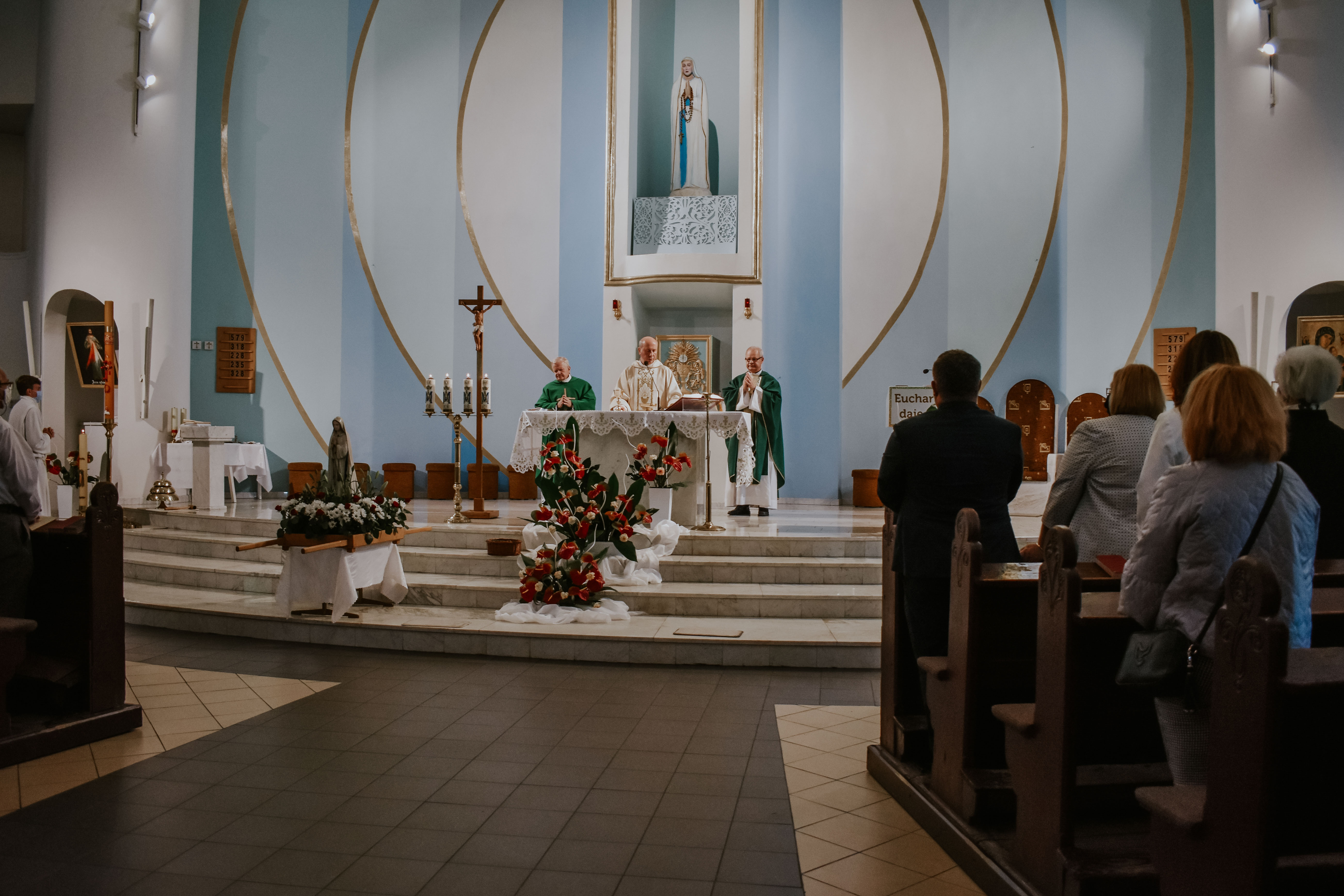 Widok na koścół od tułu i kapłan odprawający mszę świętą