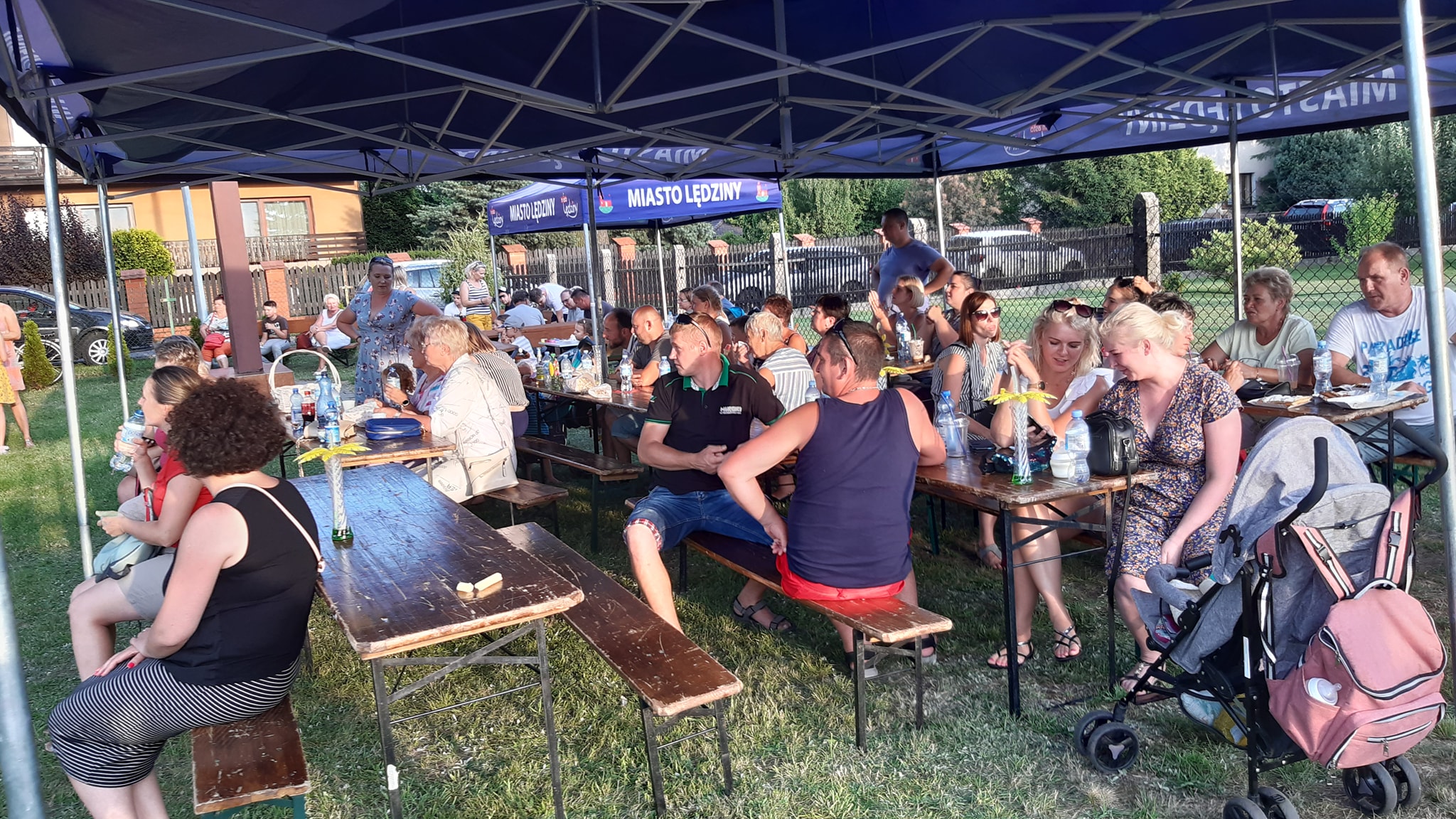 Uczestnicy pikniku siedzący przy stołach biesiadnych 