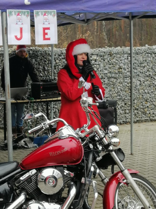 kobieta w stroju mikołaja mówi do mikrofonu. Przed nią zaparkowany jest motocykl