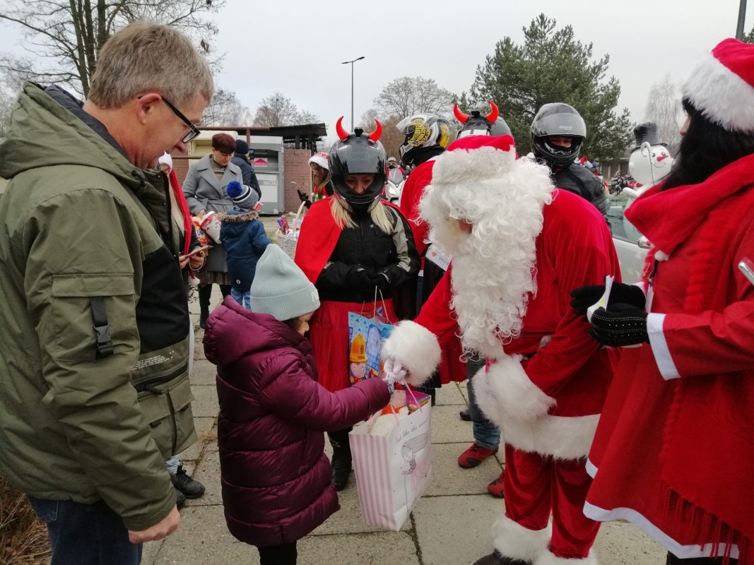 mikołaj wraz z motocyklistami przebranymi za mikołajów przekazuje dziewczynce prezent. 