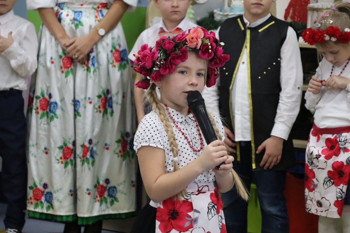 Dziewczynka w stroju regionalnym mówi do mikrofonu. Ma na głowie wianek