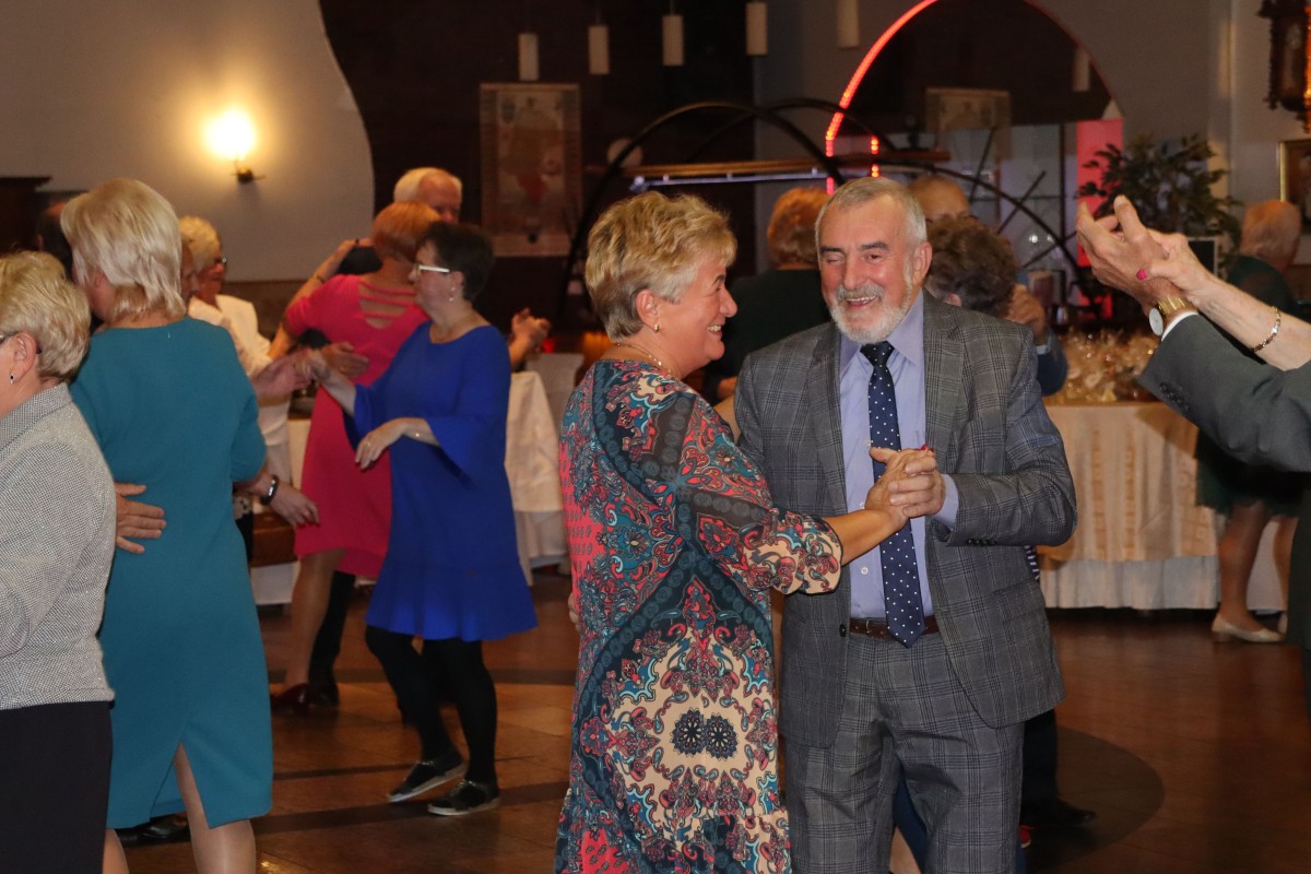 kobieta i mężczyzna tańczą na pierwszym planie. W tle tańczą inne pary