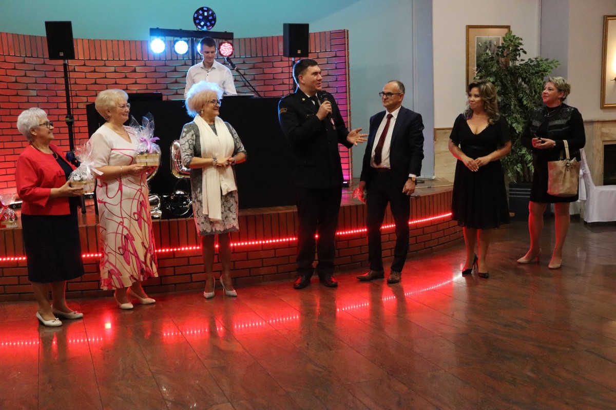 Grupa osób stojąca przed scena. Jeden z mężczyzn przemawia do mikrofonu