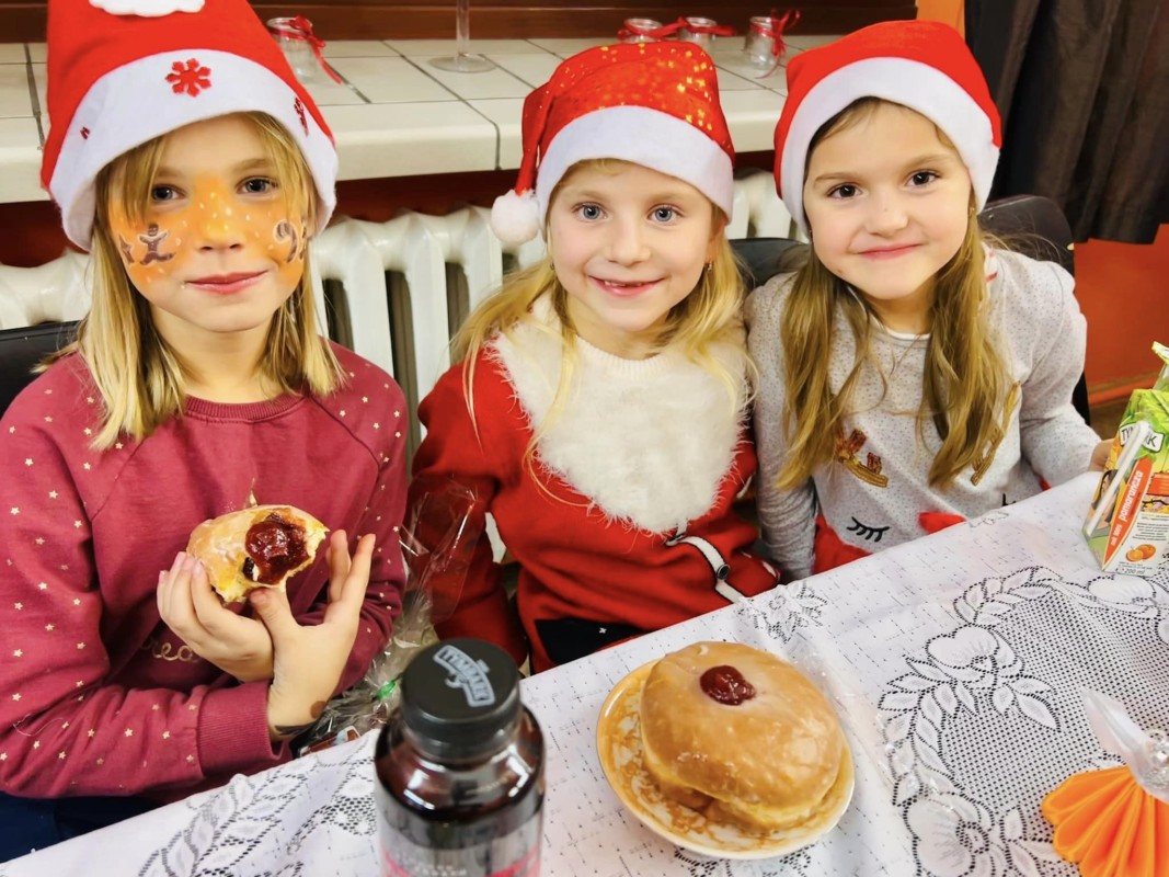 Trzy dziewczynki w czapkach mikołajowych jedzą pączki