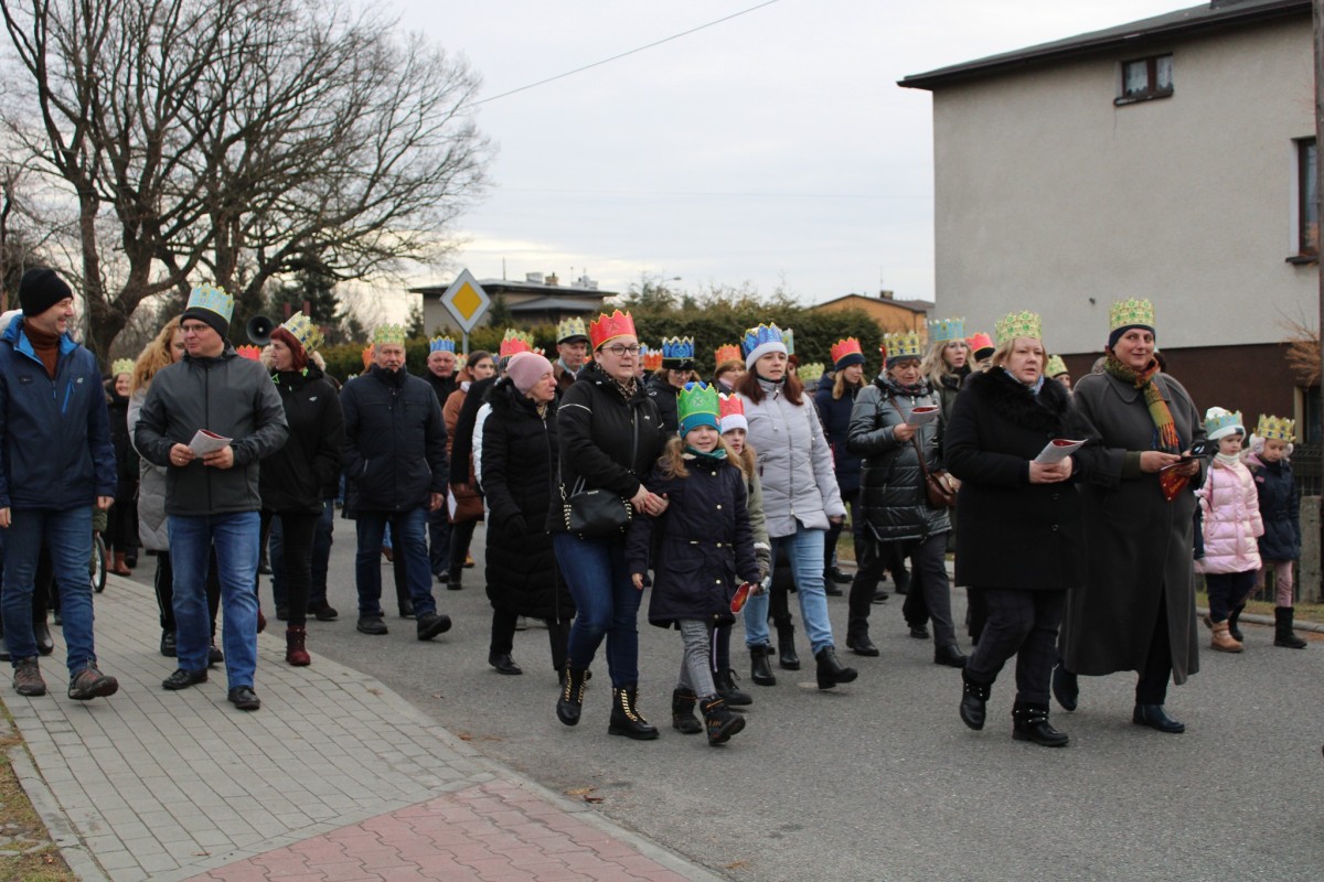 Ludzie w koronach na głowie idą ulicą podczas orszaku trzech Króli