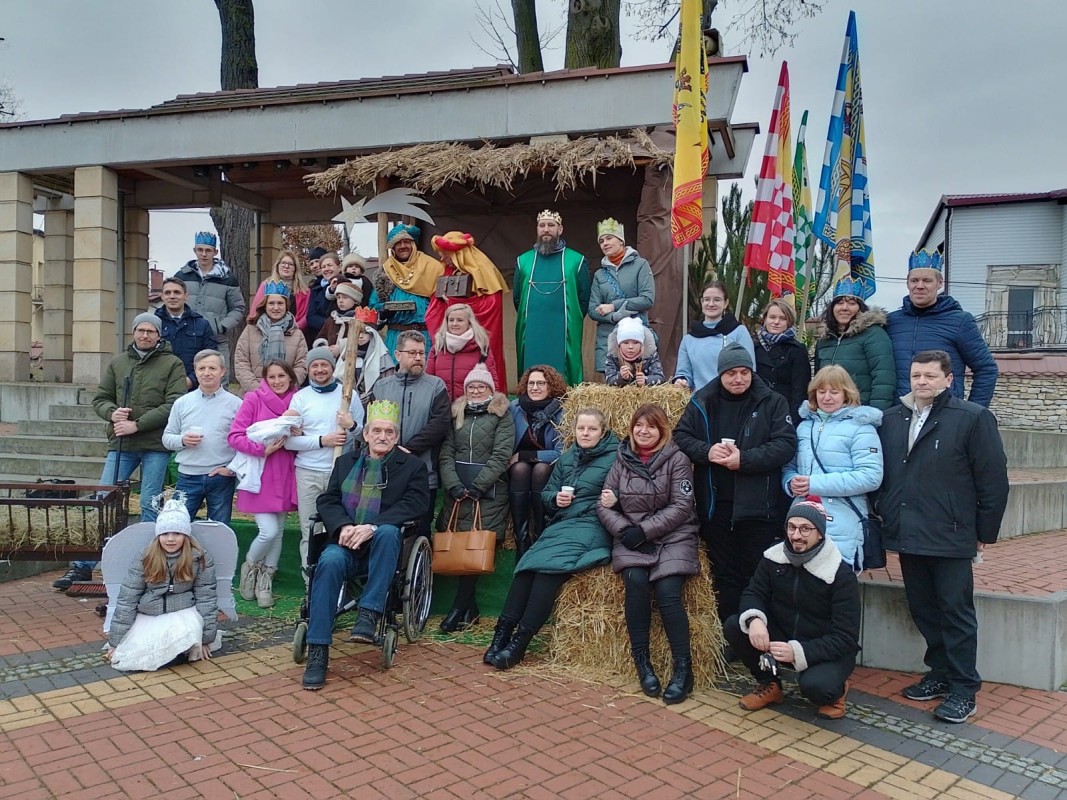 Ludzie pozują do zdjęcia podczas orszaku Trzech Króli. Stoją na scenie, część ludzi ubrana w kolorowe stroje