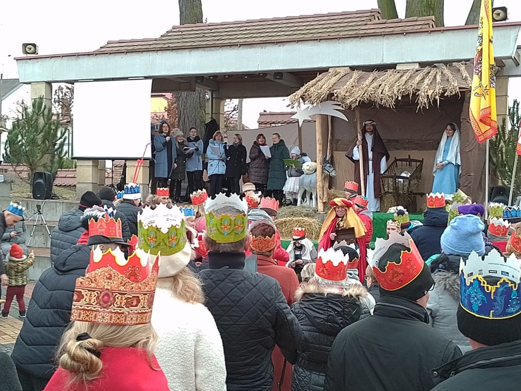 Ludzie w koronach na głowie podczas orszaku Trzech Króli. Stoją na placu Farskim w Lędzinach. Widok na scenę na której śpiewa zespół