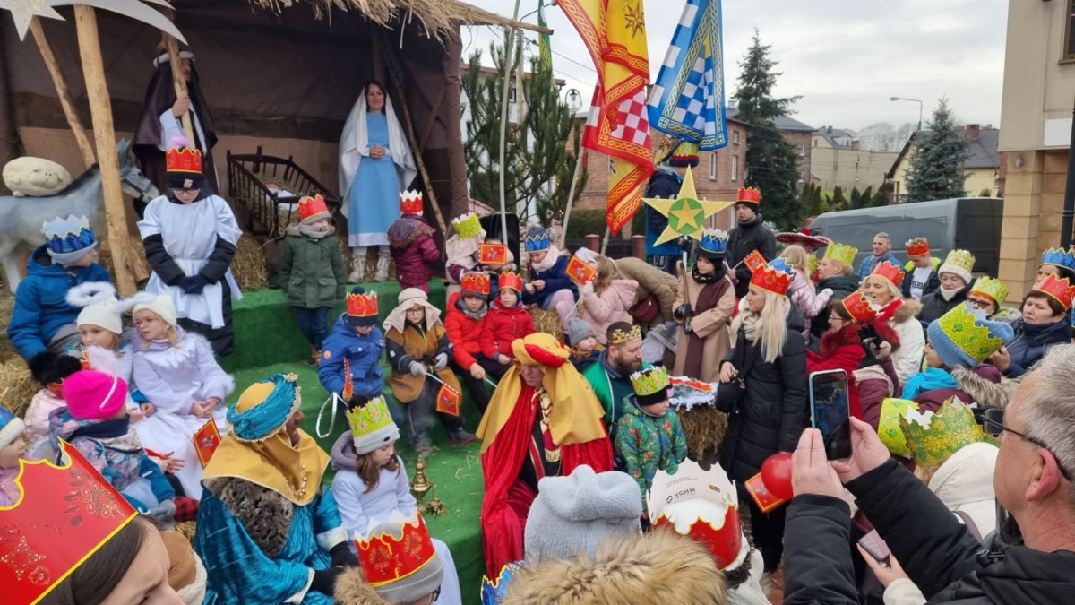 Ludzie w koronach na głowie podczas orszaku Trzech Króli. Stoją na placu Farskim w Lędzinach