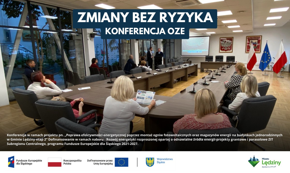 Konferencja OZE w Lędzinach. Uczestnicy siedzą przy stole konferencyjnym, prelegent stoi w tle. Na górze napis: 