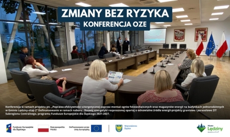 Konferencja OZE w Lędzinach. Uczestnicy siedzą przy stole konferencyjnym, prelegent stoi w tle. Na górze napis: 